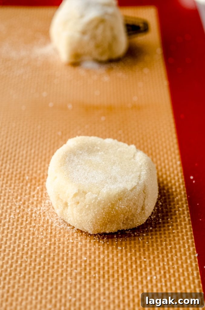 Cream Cheese Drop Cookies – Soft, Sugar Coated Treats 11 A cookie dough ball that has been flattened on a baking sheet.
