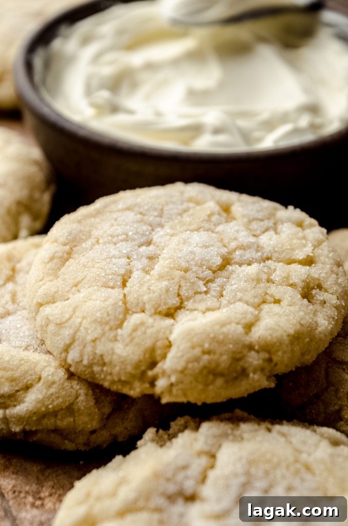Cream Cheese Drop Cookies – Soft, Sugar Coated Treats 12 Cream cheese sugar cookies on a surface with a bowl of cream cheese in the background.