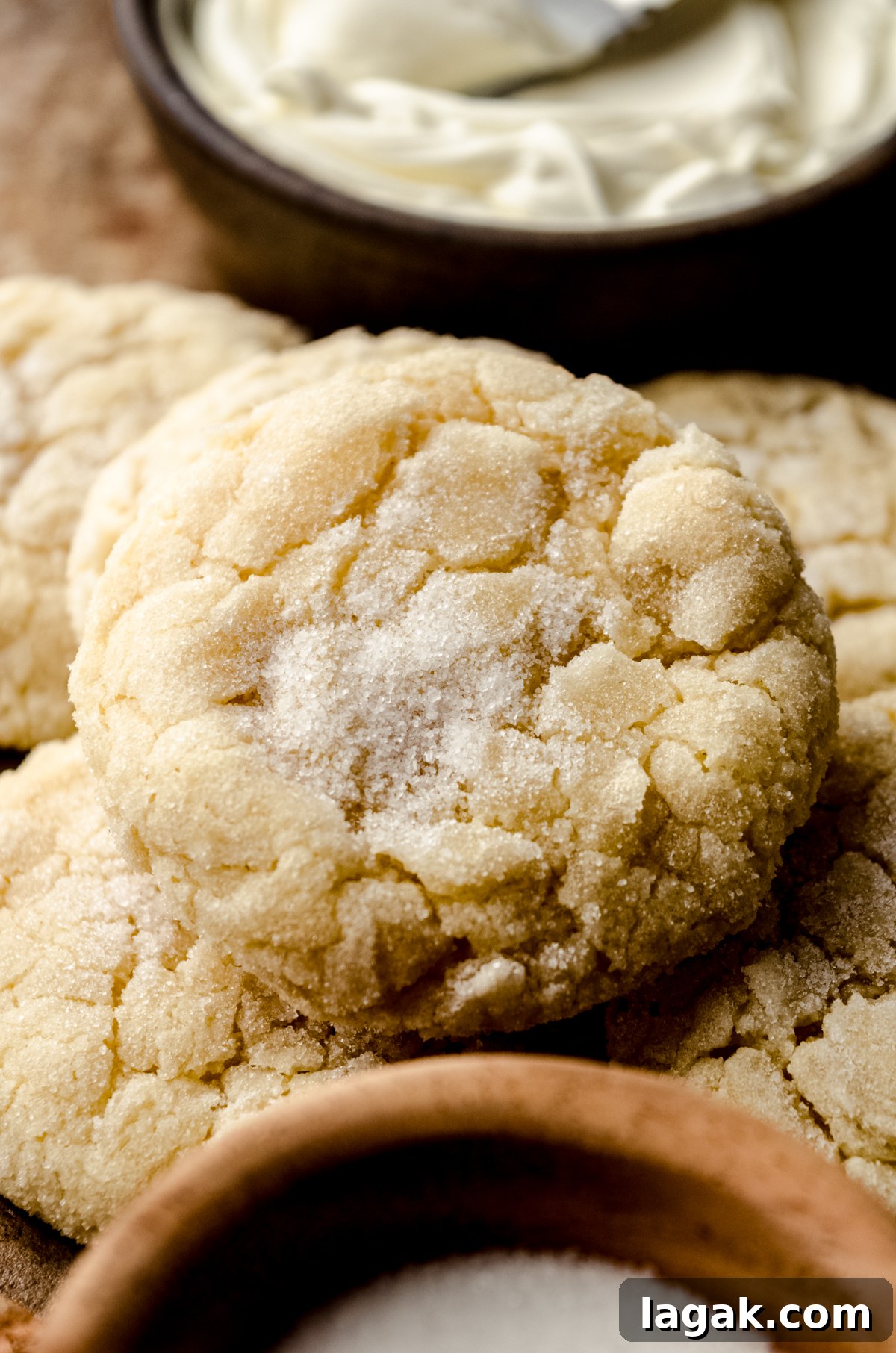 Cream Cheese Drop Cookies – Soft, Sugar Coated Treats 14 Cream cheese sugar cookies on a surface and a small bowl of sugar and a bowl of cream cheese can be seen around it.