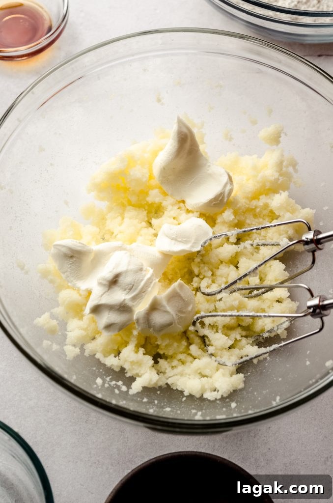 Cream Cheese Drop Cookies – Soft, Sugar Coated Treats 5 Sugar cookie dough in a bowl with chunks of cream cheese and electric beaters getting ready to mix together to make cream cheese sugar cookie dough.