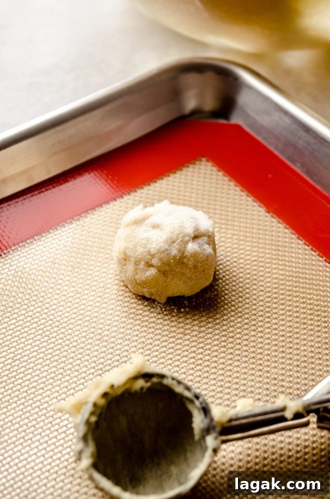 Cream Cheese Drop Cookies – Soft, Sugar Coated Treats 9 A ball of cream cheese sugar cookie dough on a baking sheet.