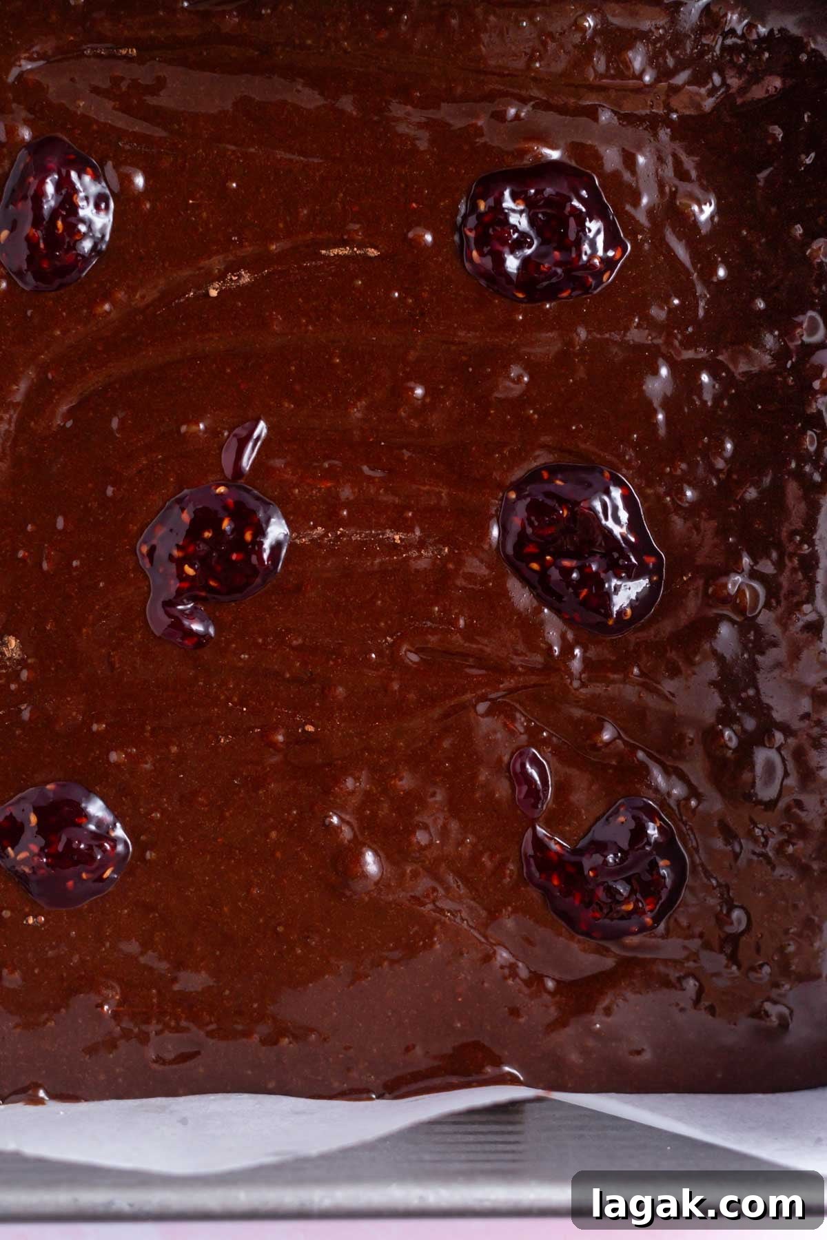 brownie batter in a baking tin with raspberry jam dolloped over the top.