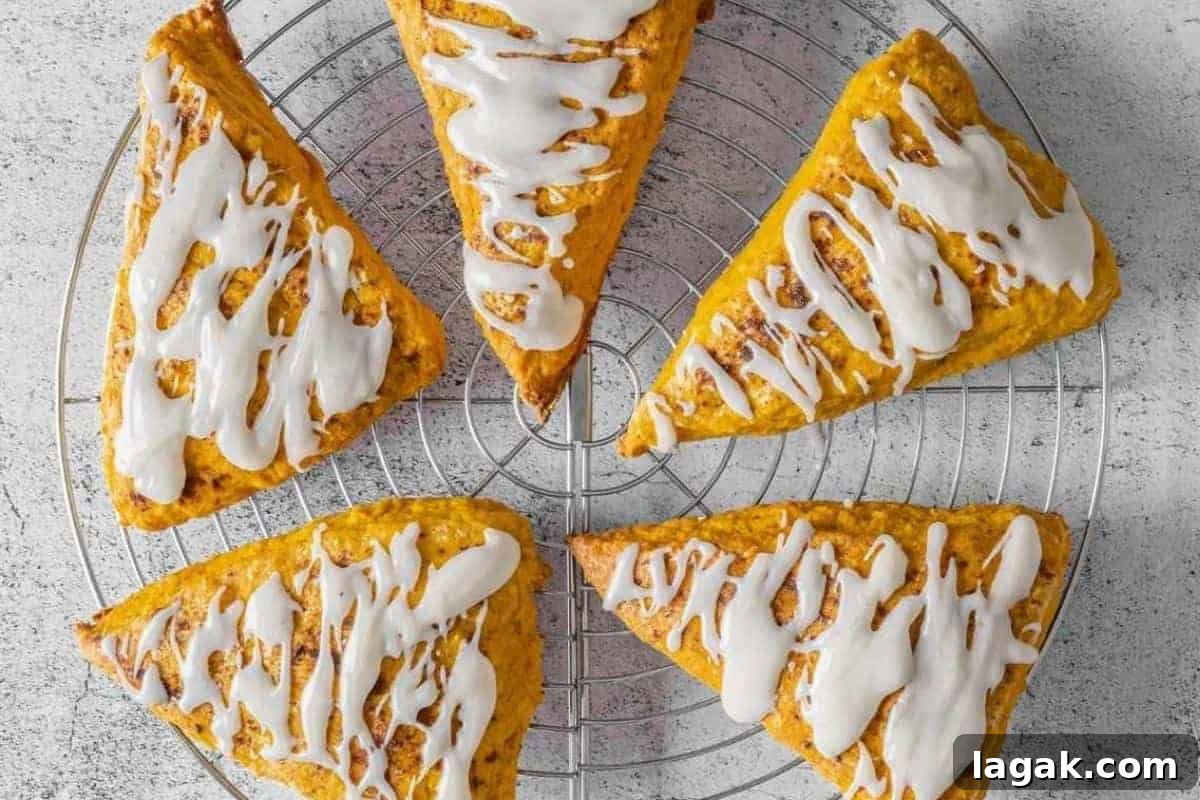 27 Cozy Fall Desserts That Taste Like Brown Sugar, Butter, and Memories 12 Five Pumpkin Spice scones with vanilla glaze are arranged in a circle on a round metal cooling rack over a light-colored surface.