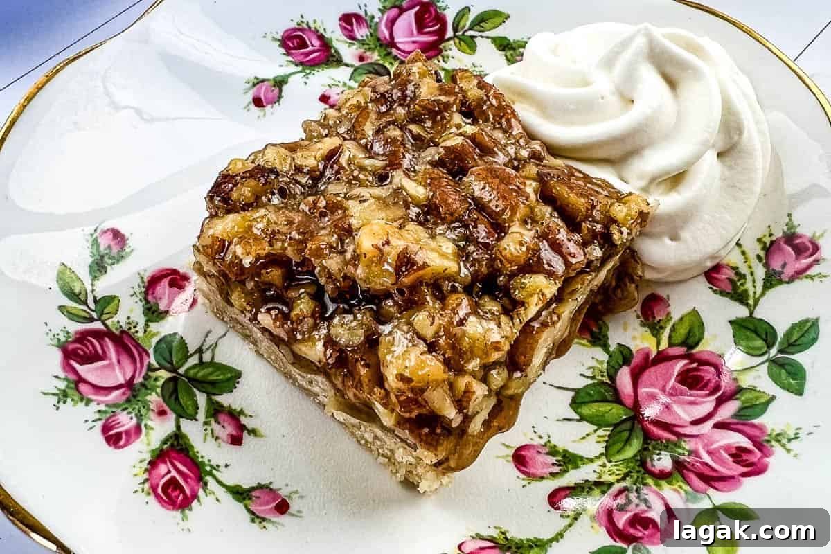 27 Cozy Fall Desserts That Taste Like Brown Sugar, Butter, and Memories 13 A slice of maple pecan pie bar topped with chopped pecans sits on a floral-patterned plate.