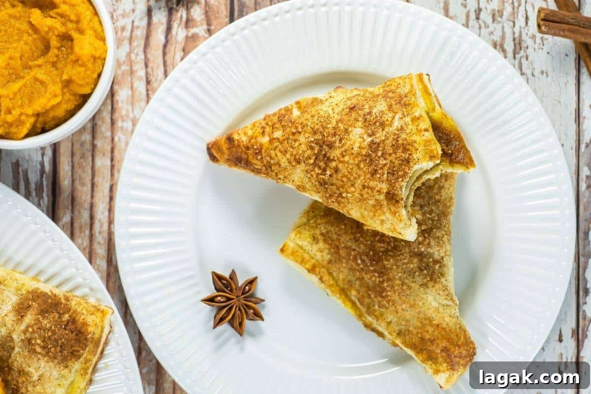 27 Cozy Fall Desserts That Taste Like Brown Sugar, Butter, and Memories 14 Pumpkin turnovers on a white plate, golden brown with spiced sugar topping and pumpkin filling peeking through.