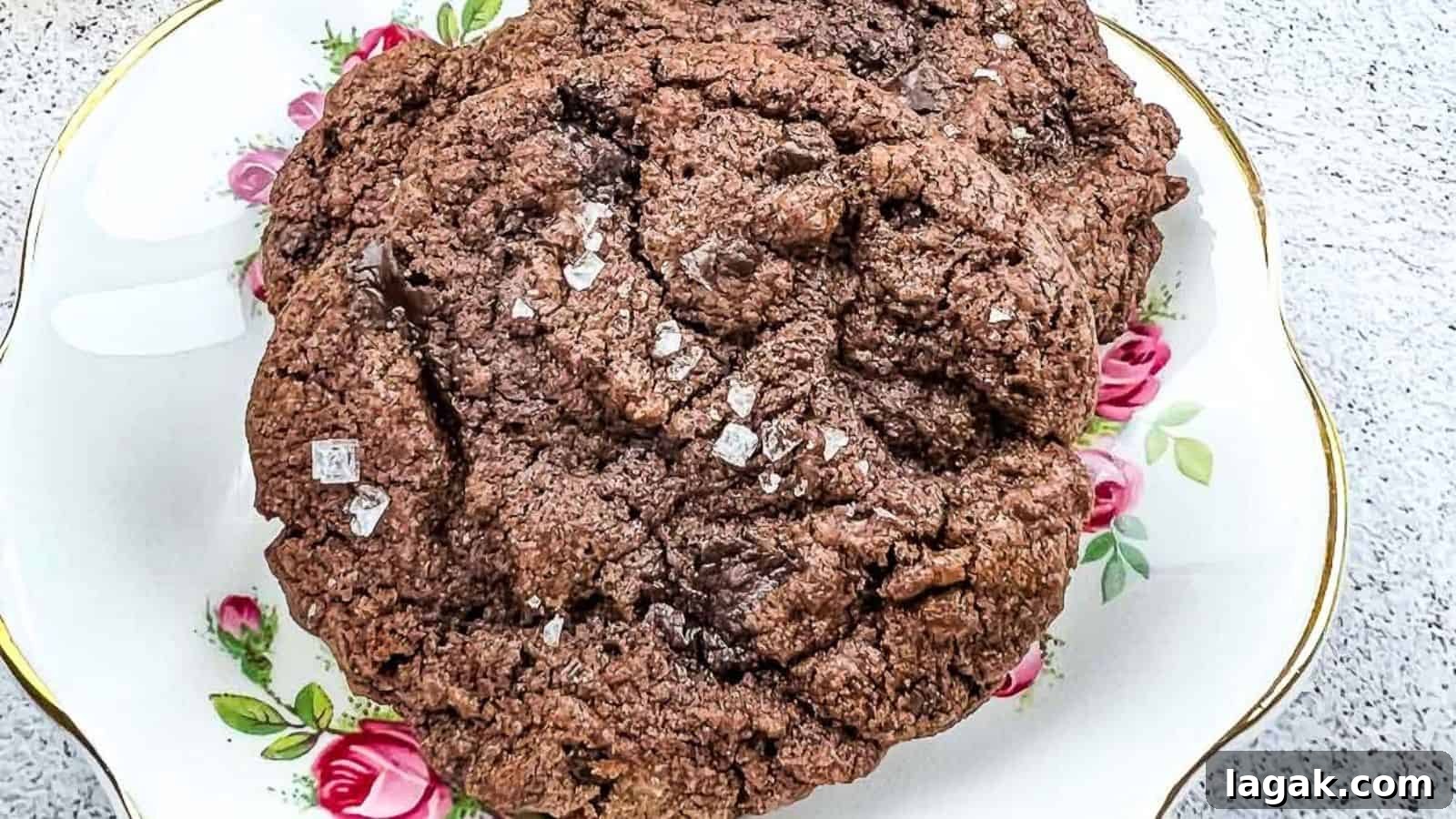 27 Cozy Fall Desserts That Taste Like Brown Sugar, Butter, and Memories 15 A close-up of a large chocolate cookie sprinkled with coarse salt, placed on a decorative plate with pink rose patterns.