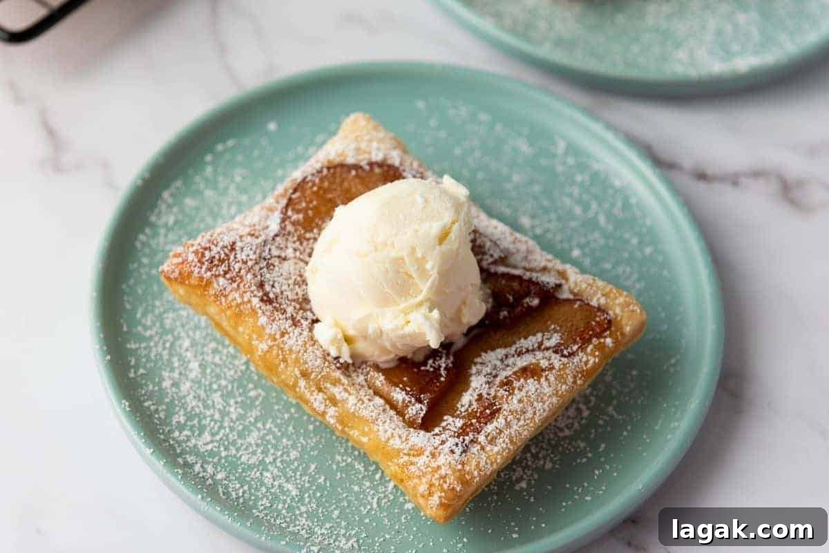 27 Cozy Fall Desserts That Taste Like Brown Sugar, Butter, and Memories 17 A Puff Pastry Apple Tart topped with a scoop of vanilla ice cream and sprinkled with powdered sugar sits on a light green plate.
