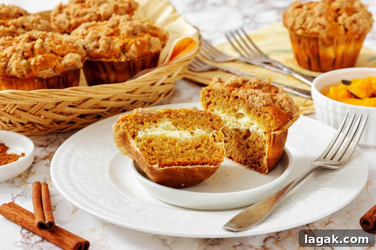 27 Cozy Fall Desserts That Taste Like Brown Sugar, Butter, and Memories 18 A Pumpkin Cream Cheese Muffins cut in half on a plate reveals a creamy filling, with more muffins in a basket and a bowl of diced fruit in the background.