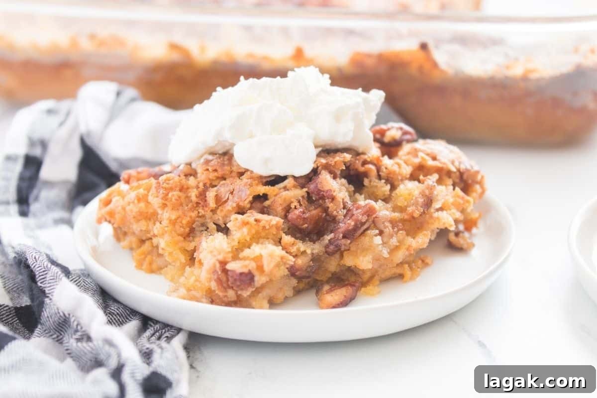 27 Cozy Fall Desserts That Taste Like Brown Sugar, Butter, and Memories 8 A slice of Pumpkin Crunch Cake on a white plate, topped with whipped cream, with a checkered cloth beside it and a baking dish in the background.