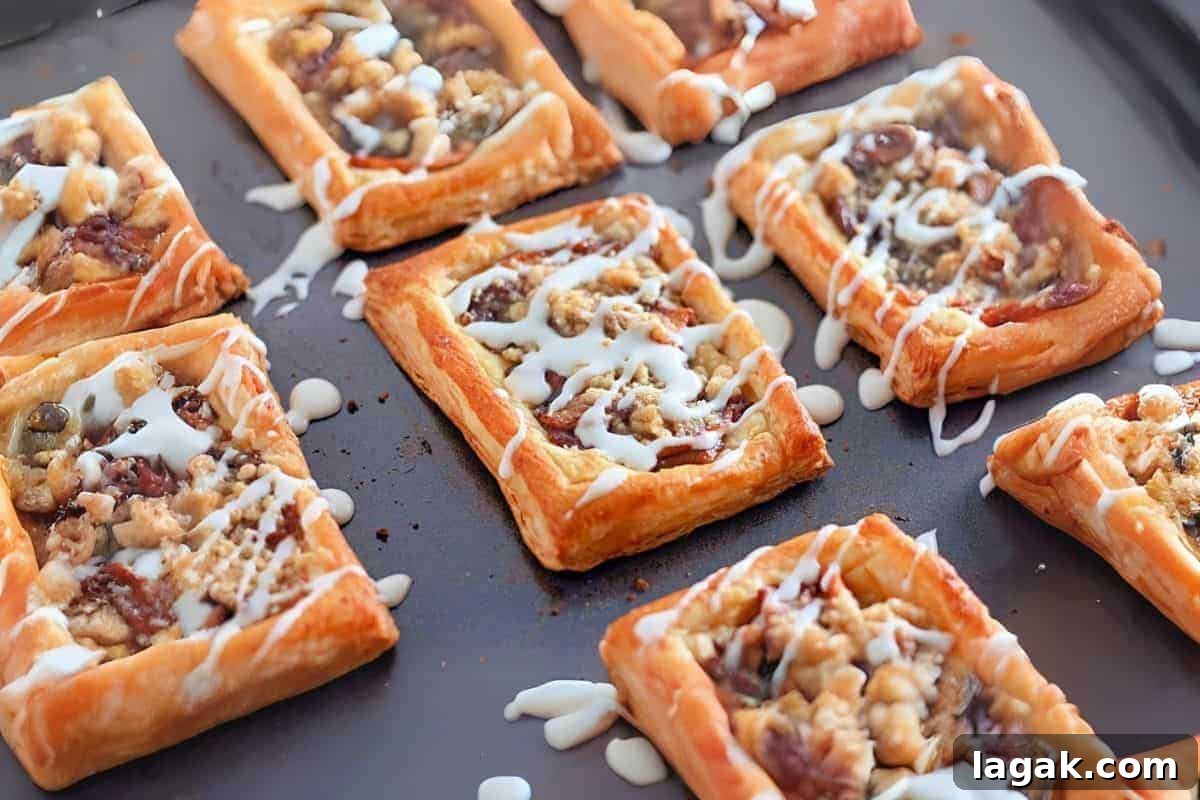 27 Cozy Fall Desserts That Taste Like Brown Sugar, Butter, and Memories 9 Golden brown Dutch Apple Danishes, topped with a fruit and nut filling, drizzled with white icing, displayed on a dark baking sheet.