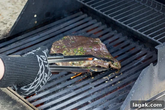 Asian-Inspired Gluten-Free Steak Marinade Recipe for Bold Flavor 4 A gluten free flank steak being placed on a hot grill metal tongs.