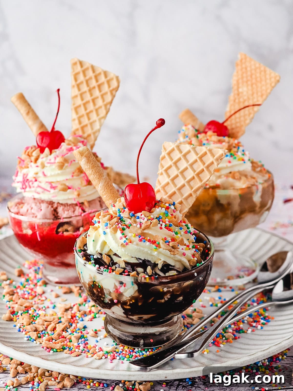 Group of three sundaes, classic, strawberry and caramel, with whipped cream, nuts, sprinkles, wafers and cherry, on a plate with spoons, nuts and sprinkles.