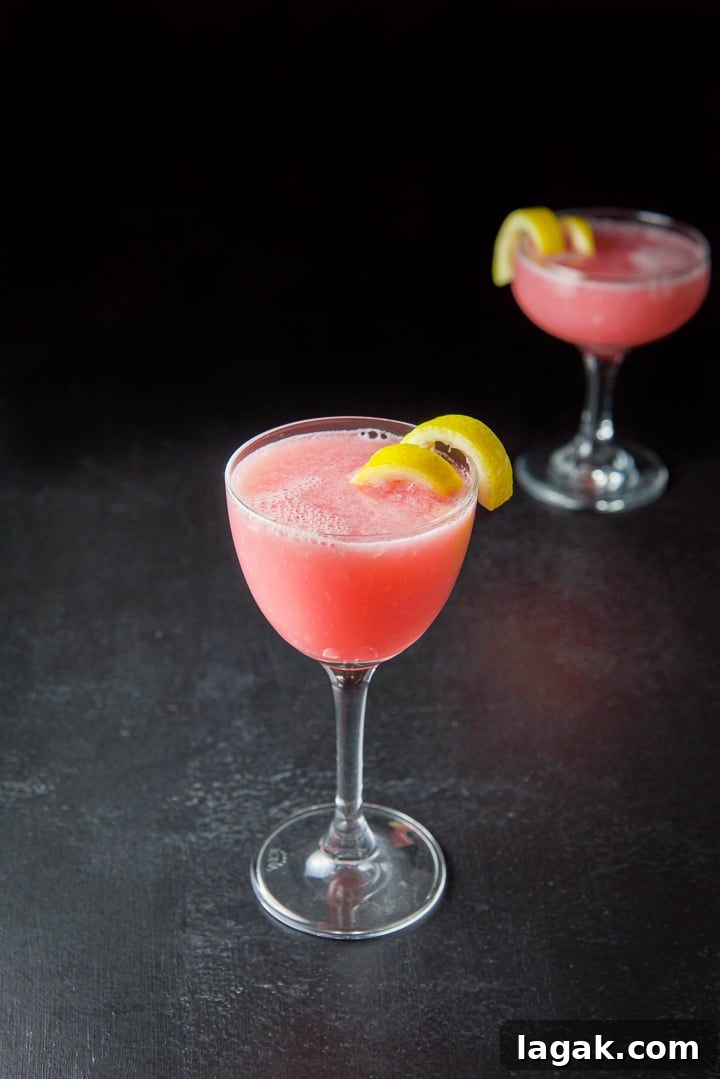 Pink Lady Cocktail Recipe: Classic Gin & Apple Cider Drink 11 Tall martini glass in front filled with the cocktail with lemon twists as garnish
