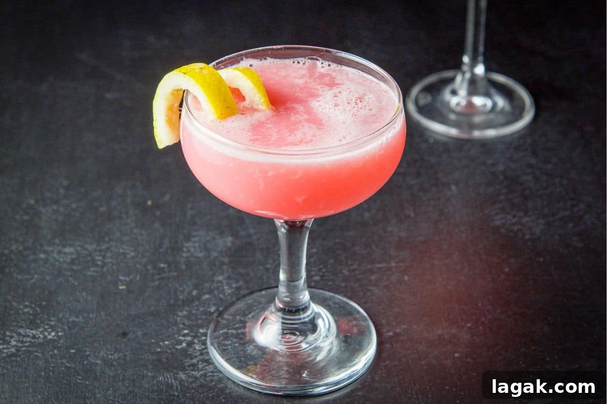 Pink Lady Cocktail Recipe: Classic Gin & Apple Cider Drink 3 a coupe glass filled with a pink cocktail and a lemon twist on the side of the glass