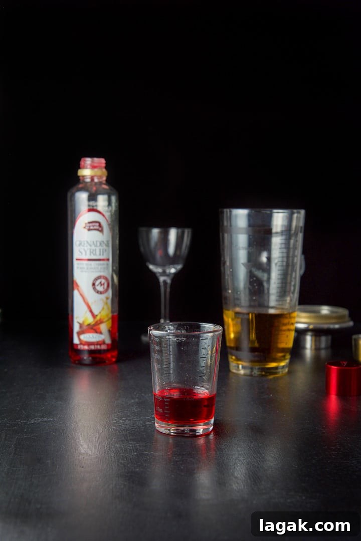 Pink Lady Cocktail Recipe: Classic Gin & Apple Cider Drink 7 Grenadine measured out with the bottle, shaker and glasses in the background