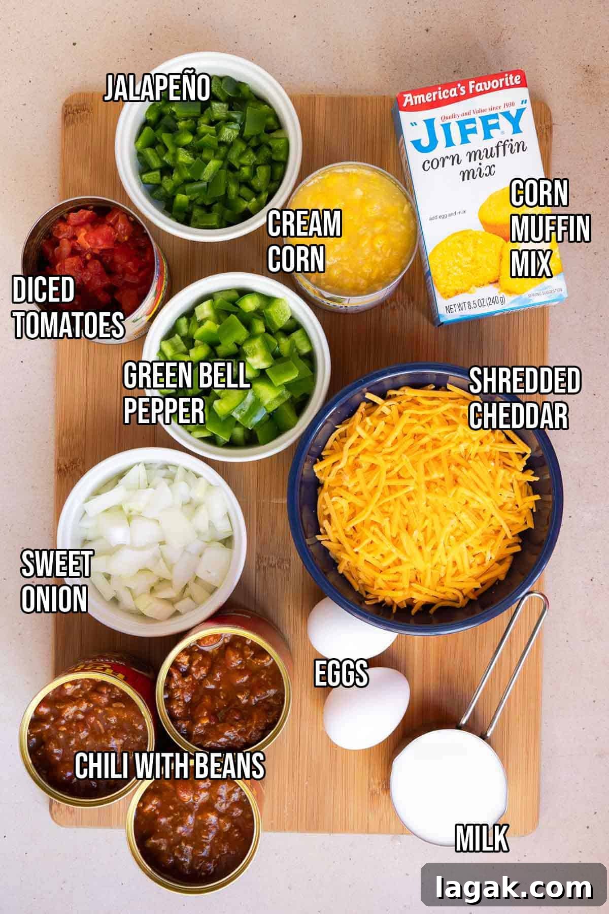 Chili cornbread casserole ingredients including canned chili with beans, fresh jalapeño, canned diced tomatoes, diced green bell pepper, diced sweet onion, shredded cheddar, a box of Jiffy corn muffin mix, canned cream style corn, eggs, and milk.