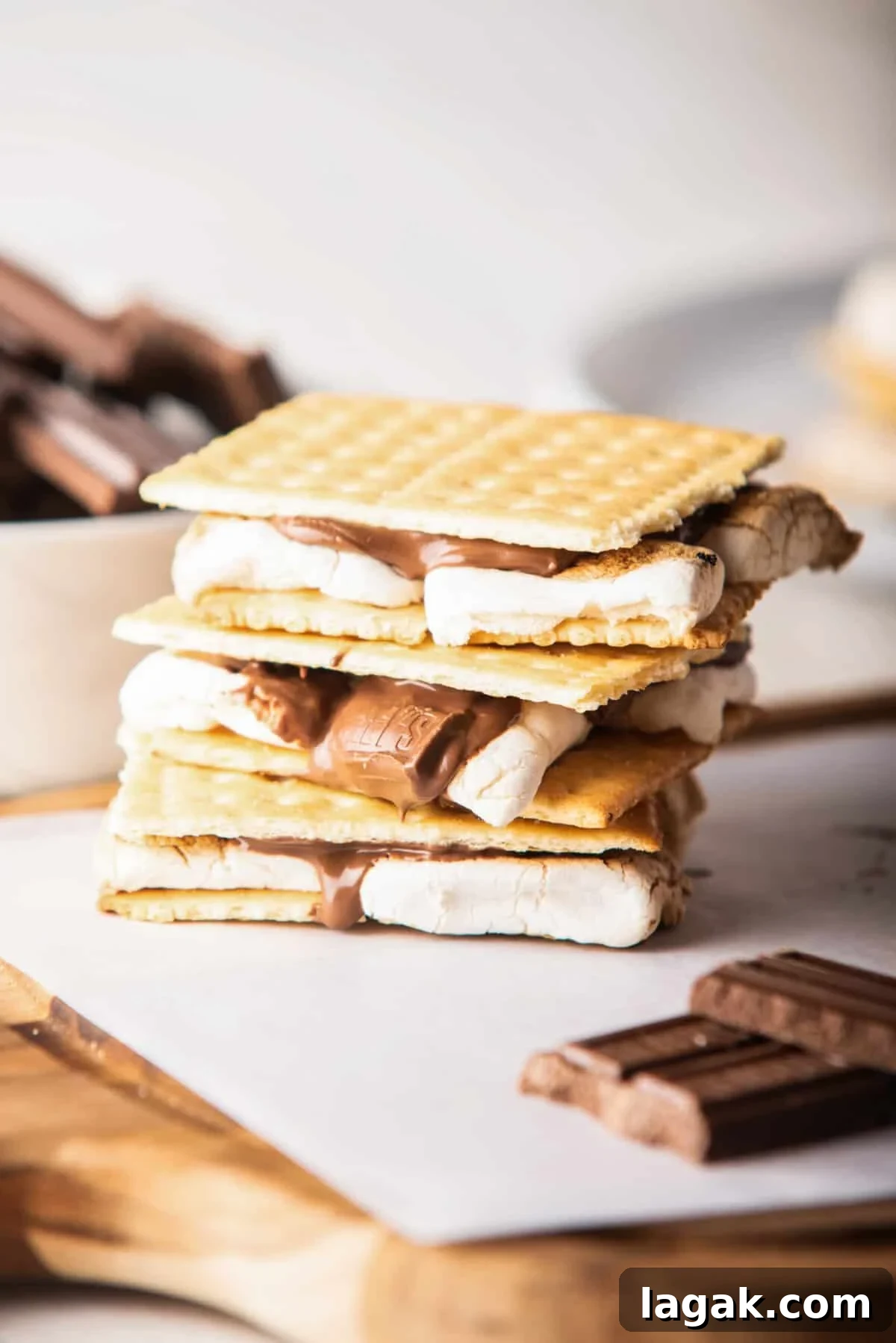 Air Fryer S'mores: Quick Indoor Campfire Dessert Recipe 2 A straight view of cooked air fryer s'mores above a wooden board next to pieces of chocolate.