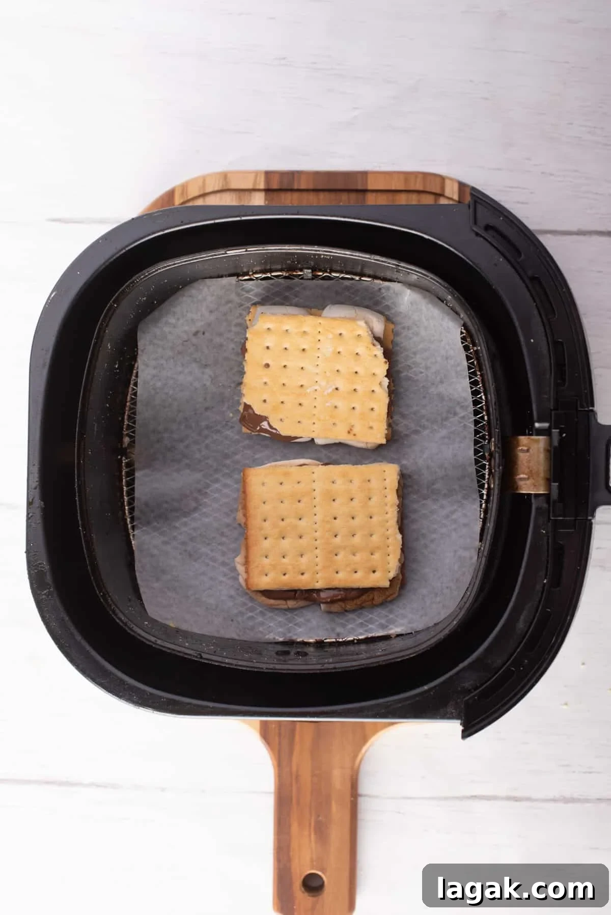Air Fryer S'mores: Quick Indoor Campfire Dessert Recipe 8 Overhead view of two Graham crackers filled with chocolate and marshmallows placed on an air fryer basket.