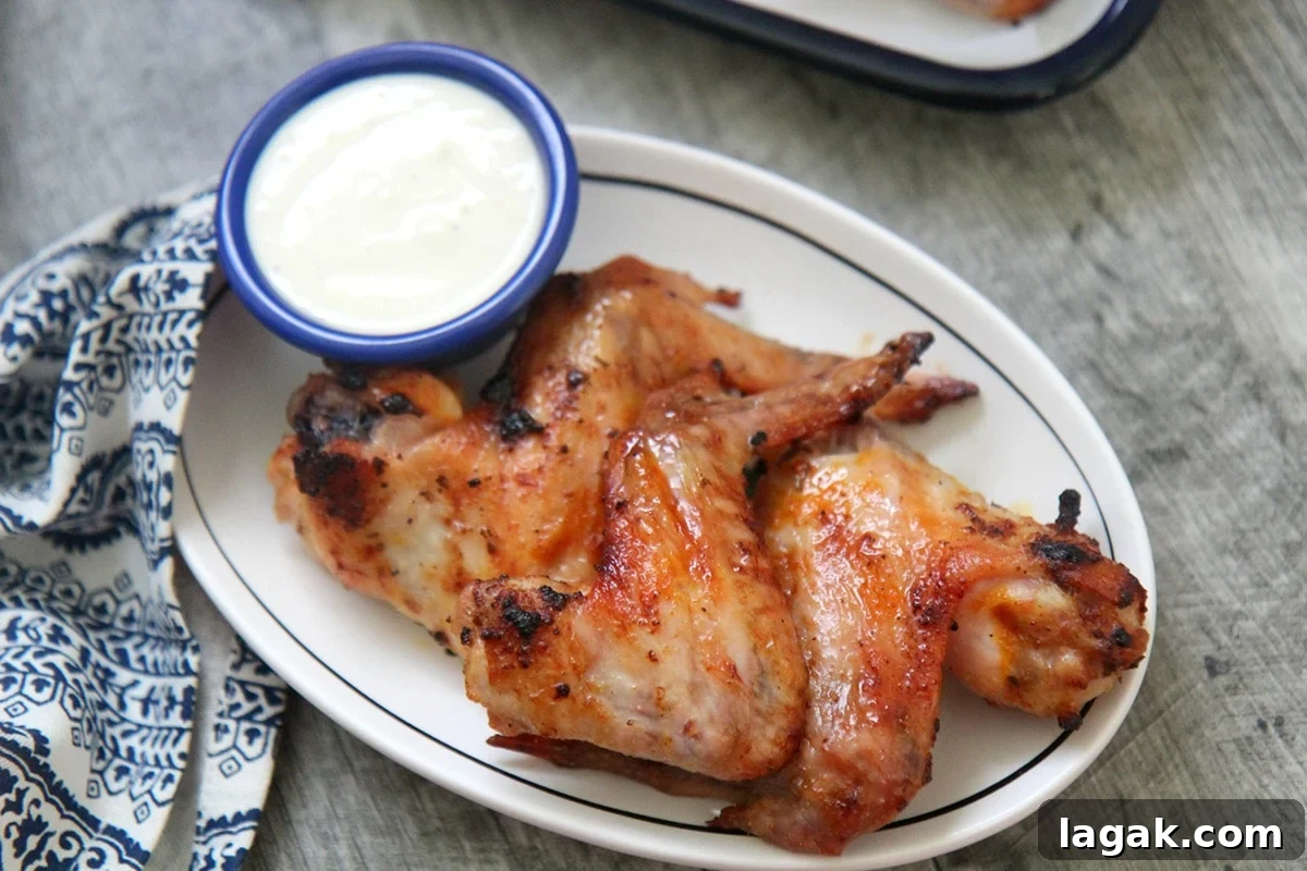 three wings on a white plate with a small side of dipping sauce and a blue and white towel on the side.