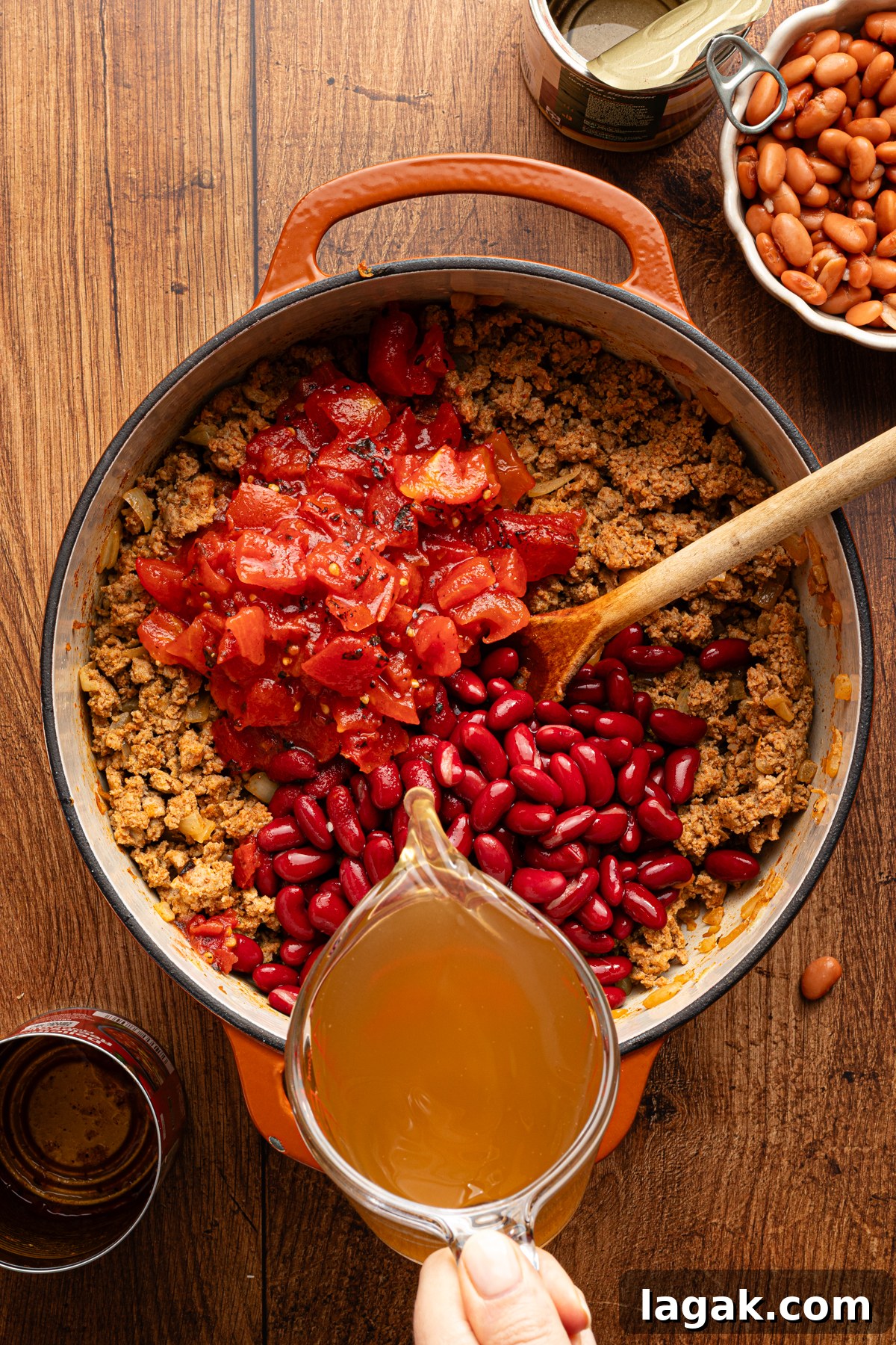 30-Minute High-Protein Turkey Chili Recipe 7 A large pot with ingredients to make 30 minute turkey chili and a person's hand pouring chicken broth into the pot