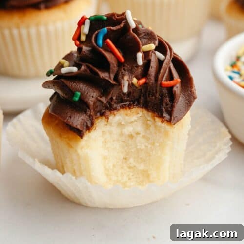 A vanilla cupcake topped with chocolate frosting and rainbow cupcakes, a bite has been taken out of the cupcake.