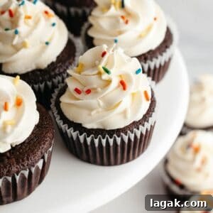 Moist Chocolate Cupcakes with Cream Cheese Frosting Recipe 17 Chocolate cupcakes with a white frosting and rainbow sprinkles on a cake stand.