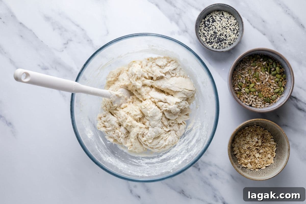 Multigrain Sourdough Bread: Step-by-Step Artisan Recipe 4 A bowl of rough mixed dough next to grains and seeds to make multigrain sourdough bread.