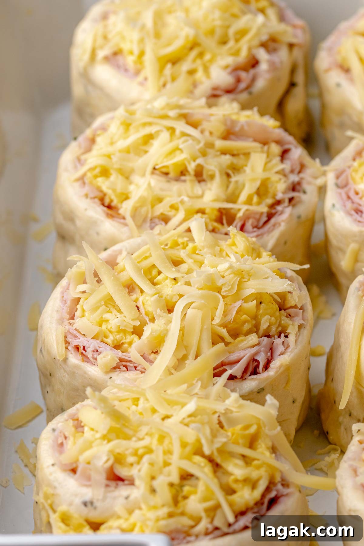 Savory Breakfast Rolls with Creamy Hollandaise Sauce 14 Savory breakfast rolls topped with shredded cheese in a casserole dish.