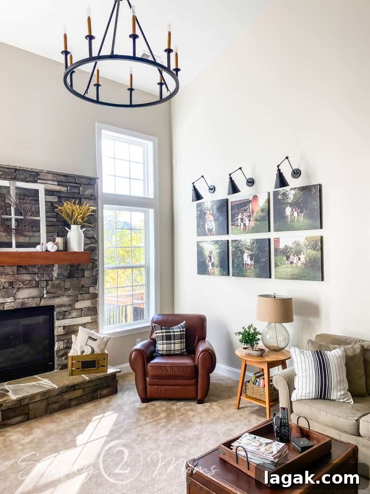 gallery wall on right side of room with light sconces above 6 large canvases. stone fireplace to left of window and family room filled with couch chair and tables