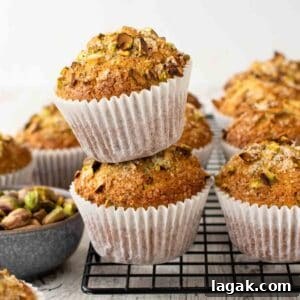 Moist Pistachio Muffins with Lemon Glaze 10 Two pistachio muffins stacked on a black wire rack with more muffins in the background.