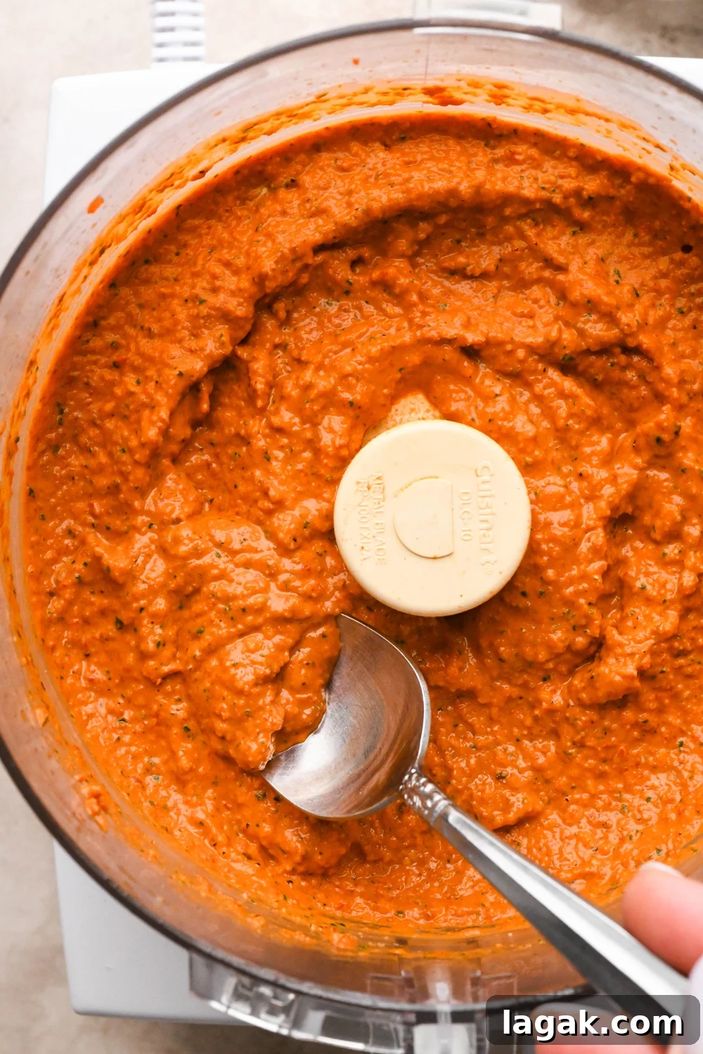 10-Minute Rustic Romesco Sauce (Dairy-Free) 5 Dairy free romesco sauce in the container of a food processor, a spoon is angled into the condiment to show the rustic yet creamy texture.