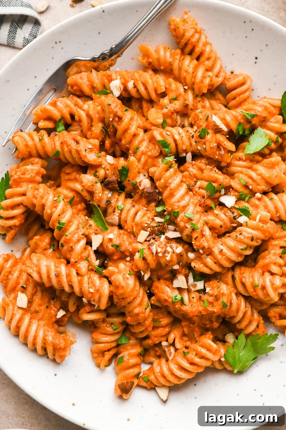 10-Minute Rustic Romesco Sauce (Dairy-Free) 10 Dairy free and gluten free romesco fusili pasta in a shallow speckled bowl, garnished with chopped almonds and fresh parsley.