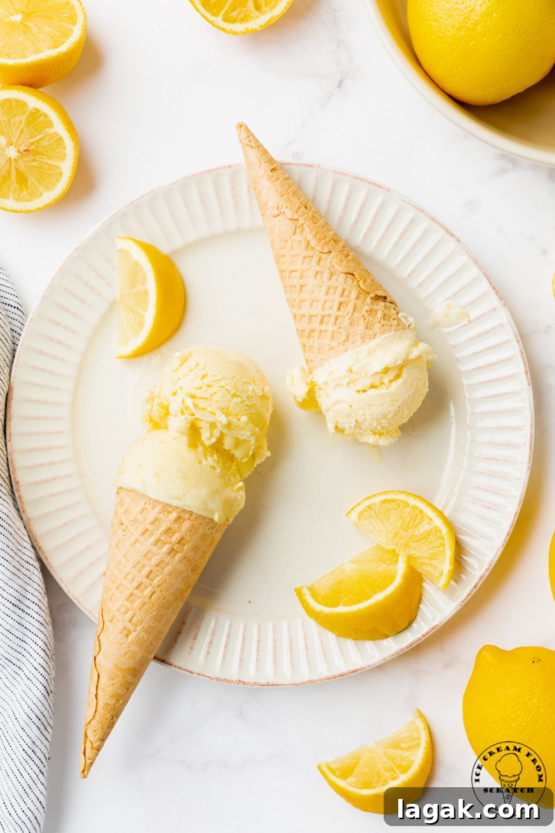 Creamy Lemon Ice Cream Recipe: Zesty Homemade Frozen Treat 6 a white fluted plate holding two sugar cones of homemade lemon ice cream, garnished with lemon wedges. Viewed from above.