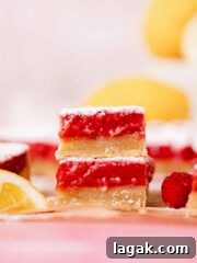two lemon raspberry squares stacked on top of each other with tangy raspberry filling and shortbread crust