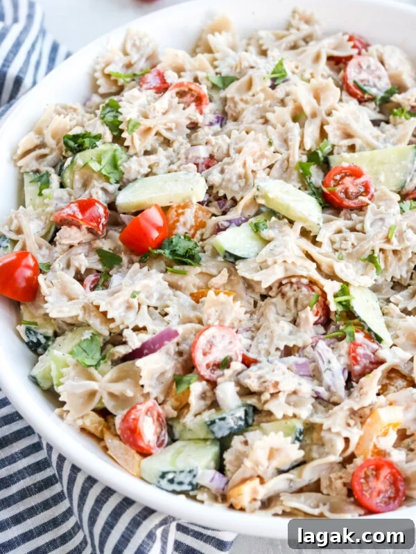 High-Protein Buffalo Tuna Salad Recipe for Meal Prep 13 Healthy tuna pasta salad in a white bowl with tomatoes, red onion, cucumbers, a mayo dressing and bowtie pasta