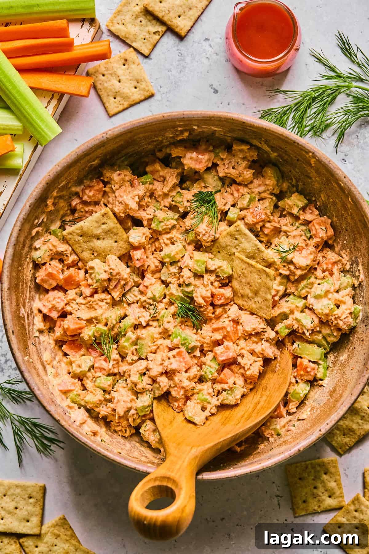 High-Protein Buffalo Tuna Salad Recipe for Meal Prep 7 buffalo tuna salad in a pink bowl with a wooden spoon surrounded by crackers and ingredients