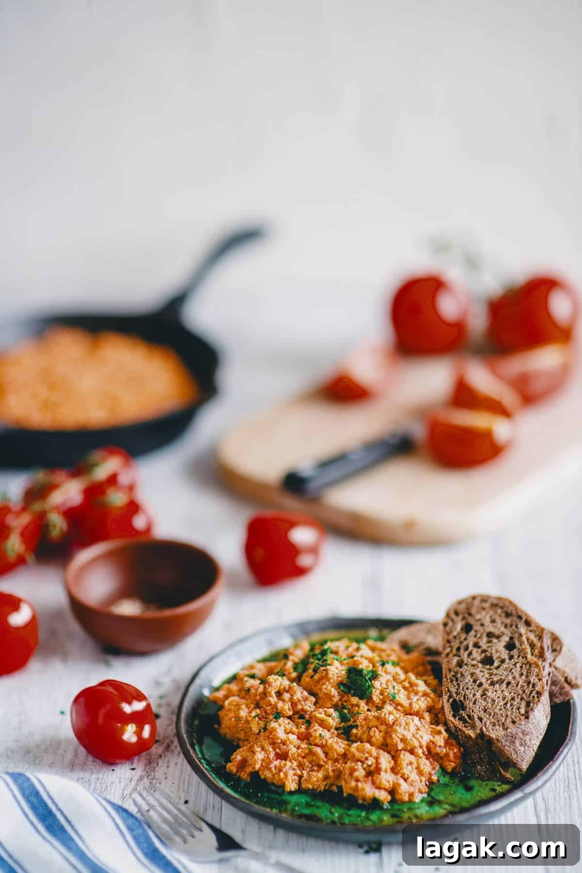 Strapatsada (Kagianas): Classic Greek Tomato Scrambled Eggs Recipe 2 Greek scrambled eggs served on a plate with fresh parsley and rustic bread, surrounded by tomatoes.