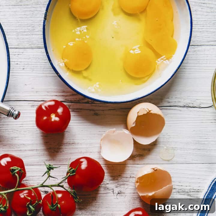Strapatsada (Kagianas): Classic Greek Tomato Scrambled Eggs Recipe 6 Bowl of cracked eggs beside fresh tomatoes on a white wooden table, ready to make Greek strapatsada.