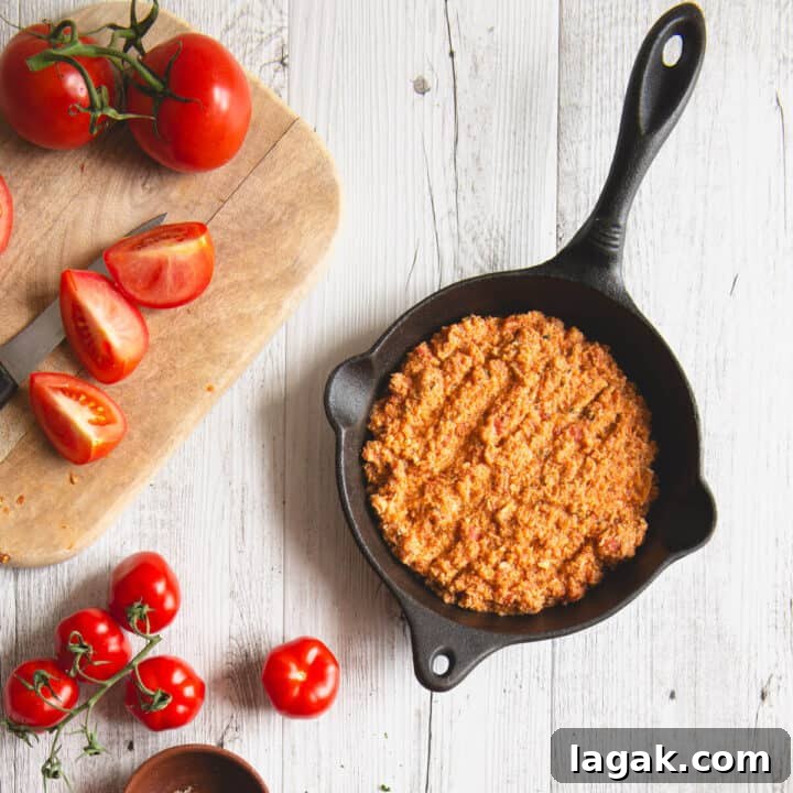 Strapatsada (Kagianas): Classic Greek Tomato Scrambled Eggs Recipe 7 Grated tomato mixture cooking in a black cast-iron skillet with fresh tomatoes on the side.