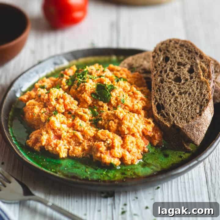 Strapatsada (Kagianas): Classic Greek Tomato Scrambled Eggs Recipe 8 Close-up of creamy Greek style scrambled eggs with tomatoes on a green plate, served with slices of dark bread.