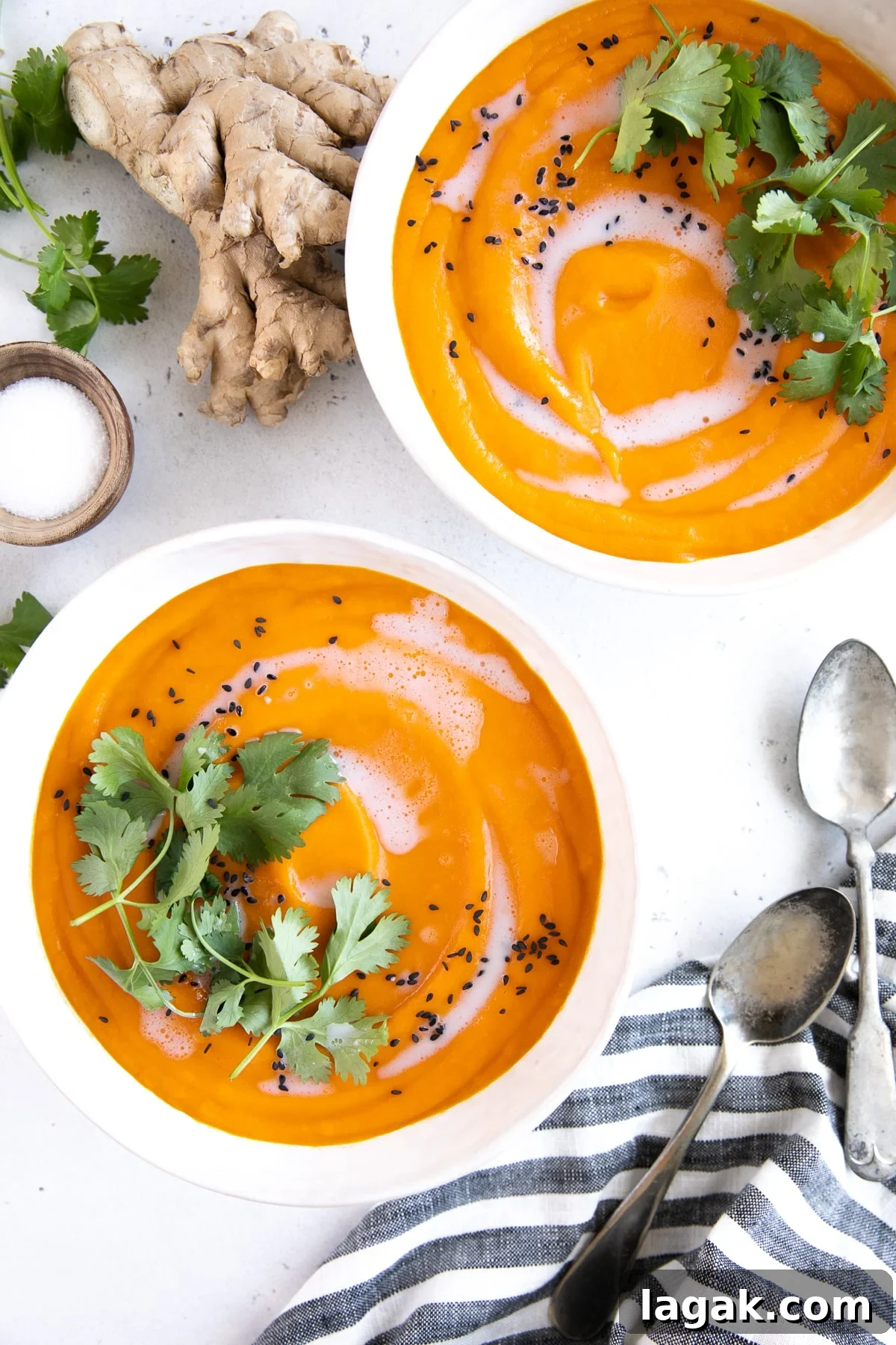 Creamy Carrot and Ginger Soup Recipe for Cozy Comfort 3 Two white soup bowls filled with ginger carrot soup and garnished with coconut cream, cilantro, and black sesame seeds.