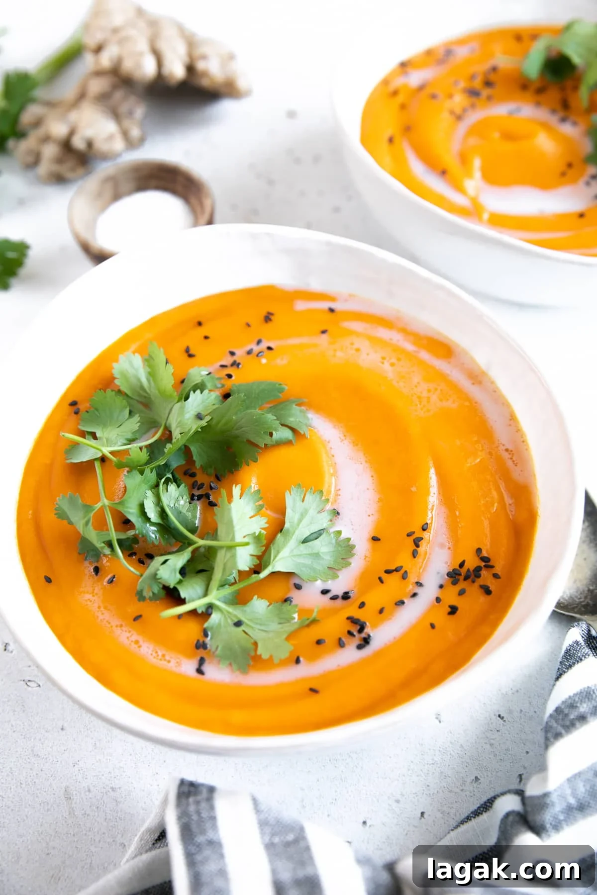Creamy Carrot and Ginger Soup Recipe for Cozy Comfort 7 Two white soup bowls filled with ginger carrot soup and garnished with coconut cream, cilantro, and black sesame seeds.