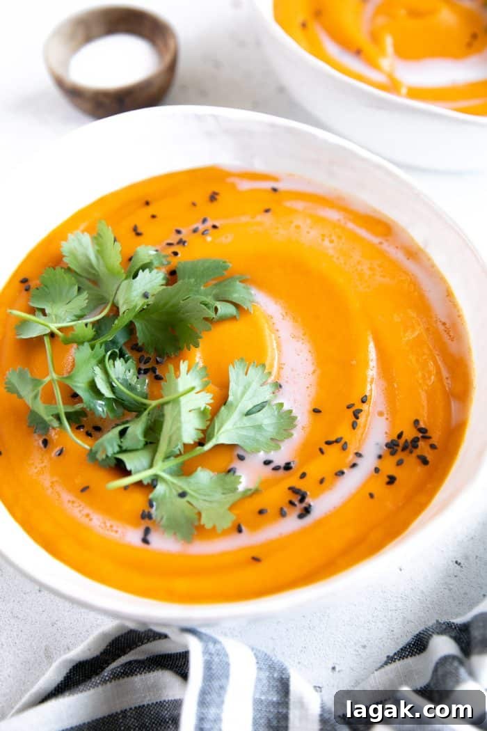 Creamy Carrot and Ginger Soup Recipe for Cozy Comfort 8 Two white soup bowls filled with ginger carrot soup and garnished with coconut cream, cilantro, and black sesame seeds.