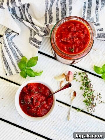 Homemade pizza sauce in a jar and in serving dish with herbs and garlic scattered around