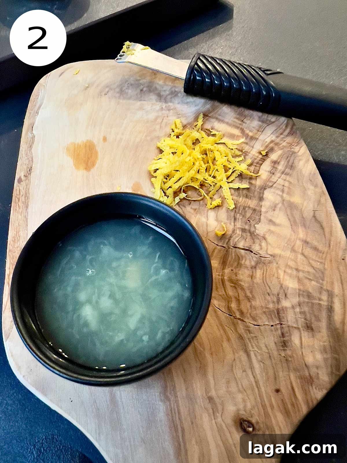 Lemon zest or lemon rind and lemon juice on a wood chopping board with a zester in the background.