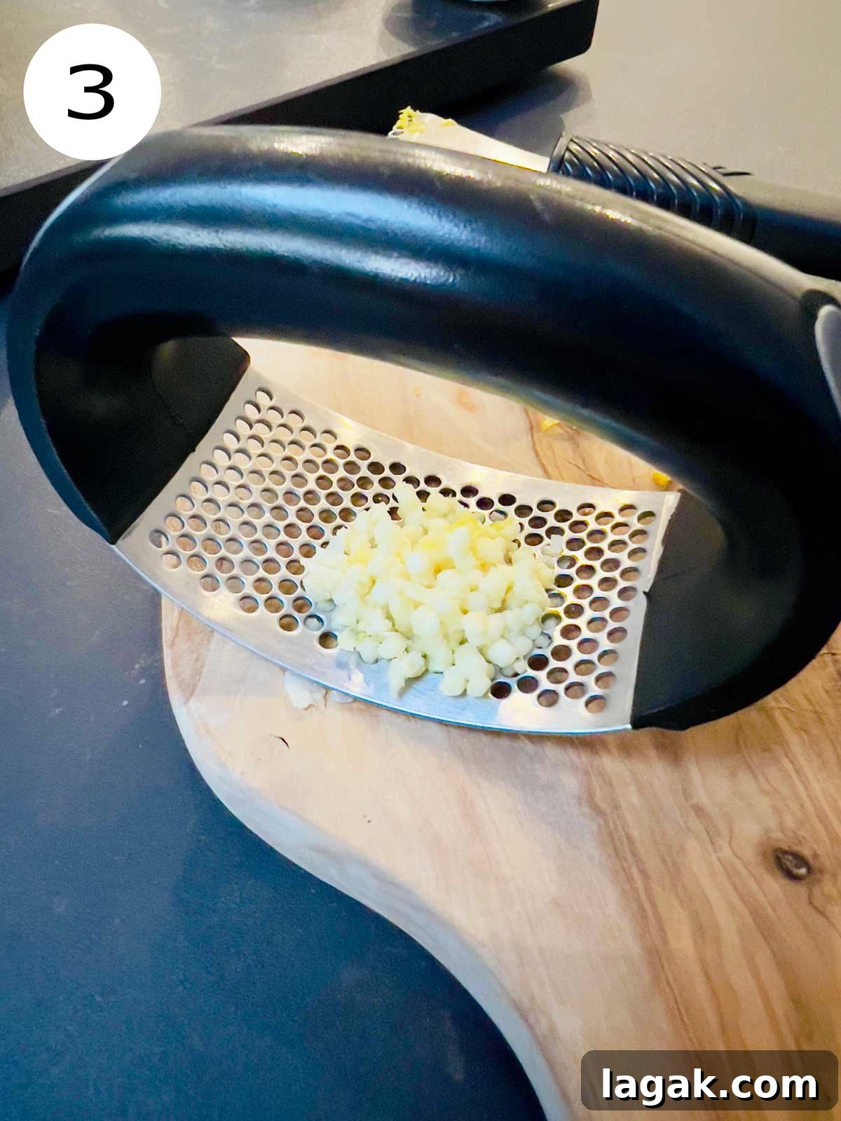 Minced garlic and garlic mincer on a chopping board.