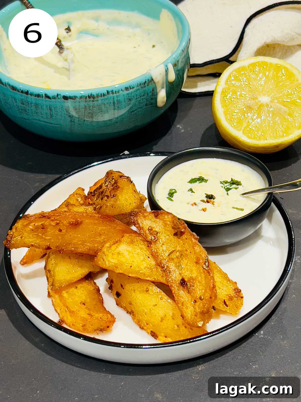 Mint and yoghurt sauce served with potato wedges on a white and black rim serving plate.