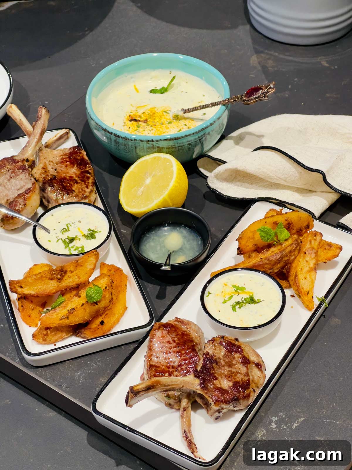 Yogur mint sauce served with lamb chops and potato wedges on two rectangular white serving plates.