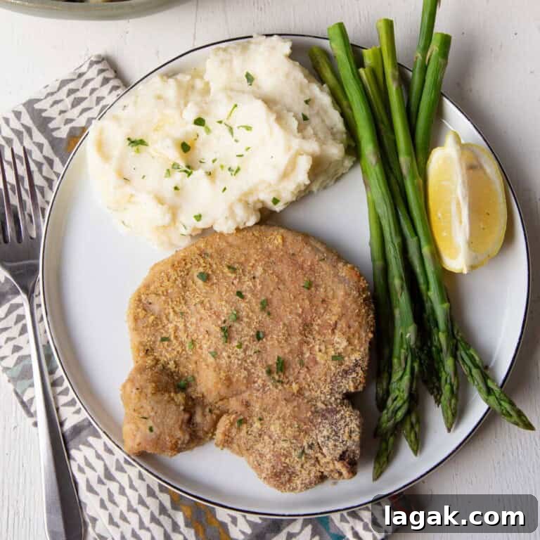 shake and bake pork chop on a plate with mashed potatoes and asparagus.