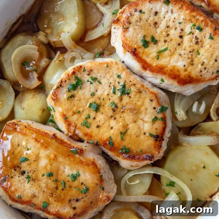 three pork chops on top of sliced potatoes and onions in a casserole dish.